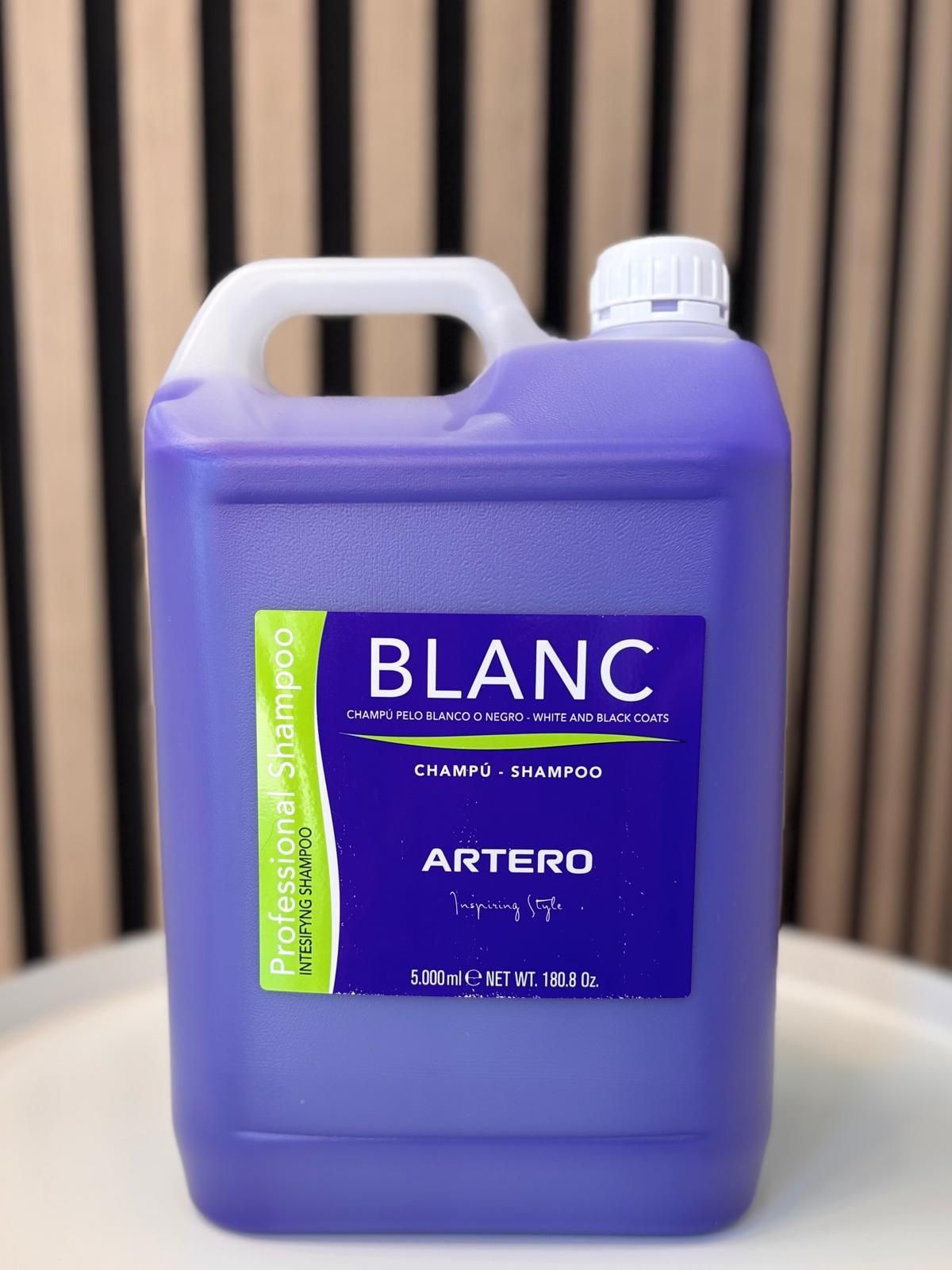 Una botella morada de champú Blanc Artero está sobre una mesa.