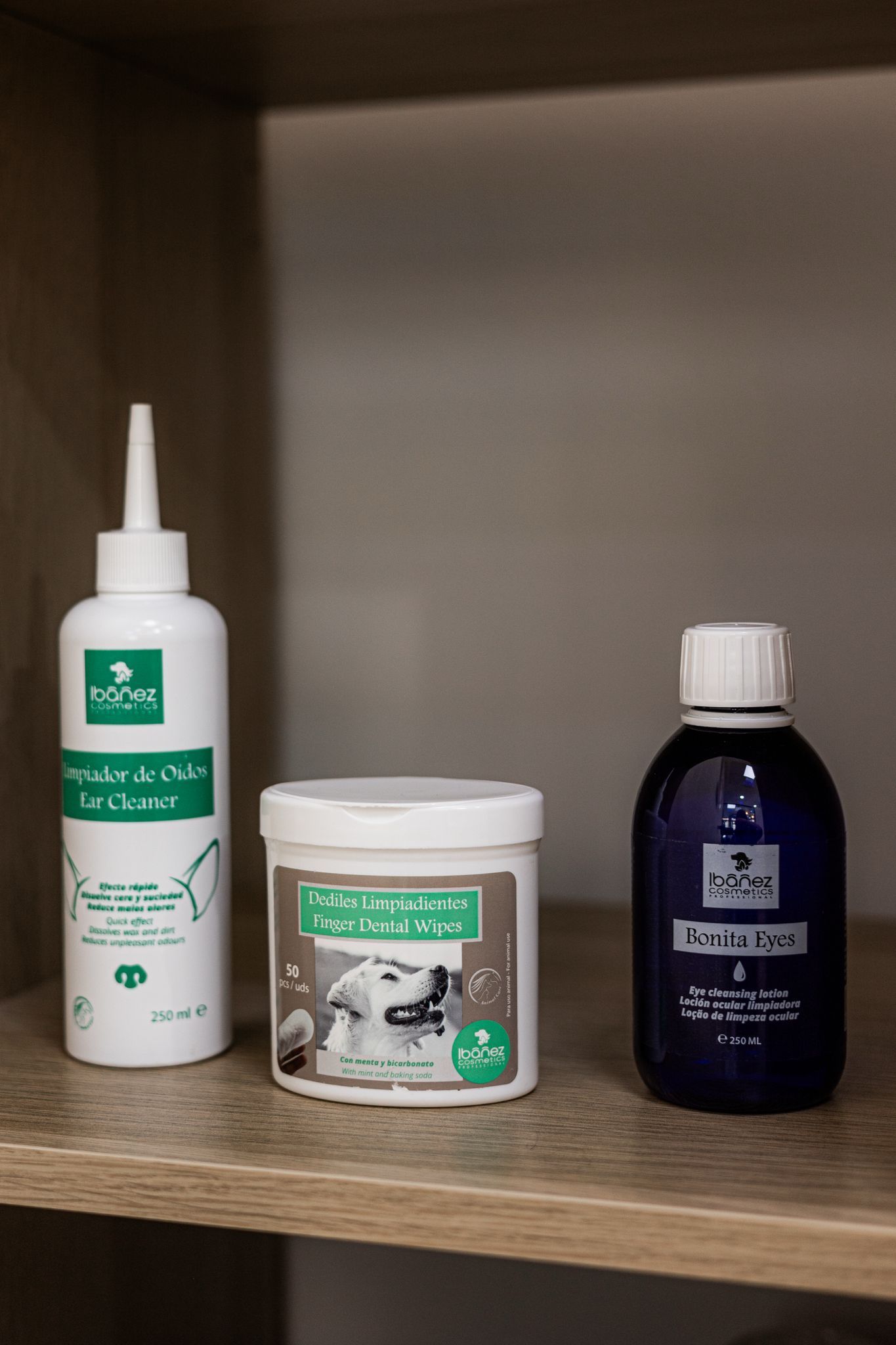 Hay tres botellas de champú para perros en un estante de madera.