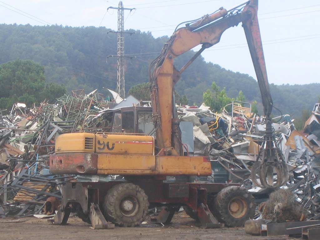 Una excavadora amarilla está sentada en una pila de chatarra.