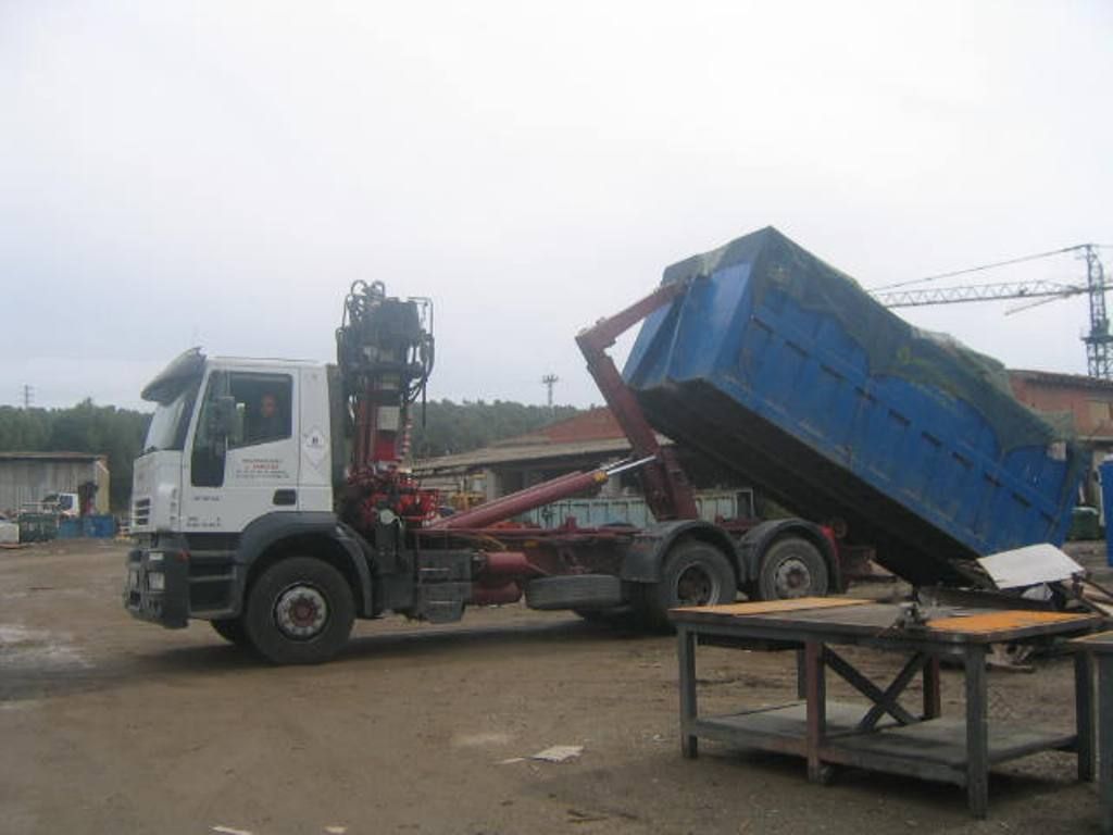 Se está cargando un contenedor de basura en un camión en un estacionamiento.