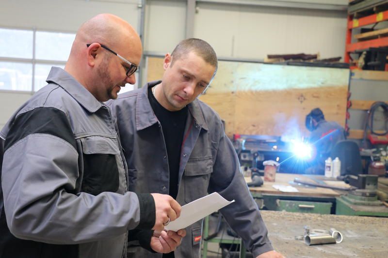 Zwei Männer schauen sich in einer Fabrik ein Stück Papier an.