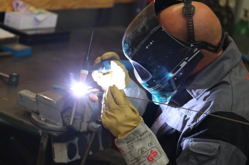 Ein Mann mit einer Schweißmaske schweißt ein Stück Metall.