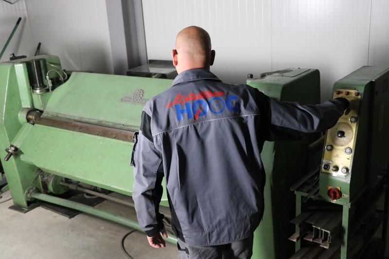 Ein Mann in einer grauen Jacke steht vor einer Maschine.