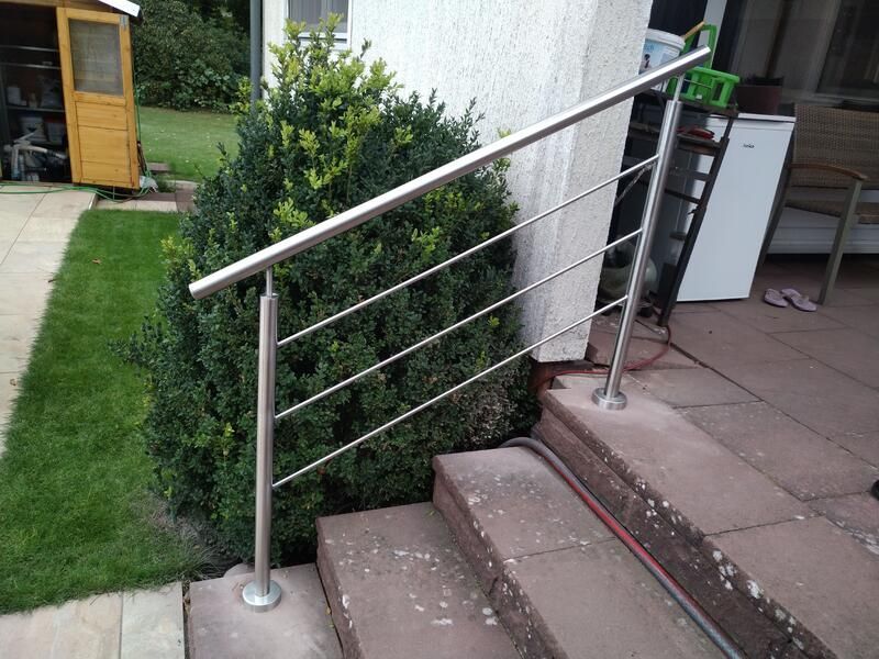 Ein Edelstahlgeländer an einer Treppe neben einem Busch.