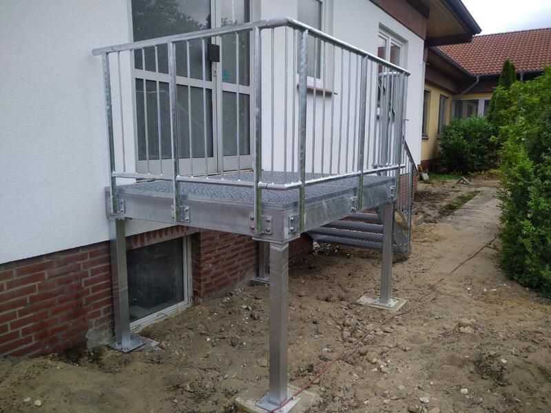 An der Seite eines Hauses wird ein Metallbalkon mit Treppe gebaut.