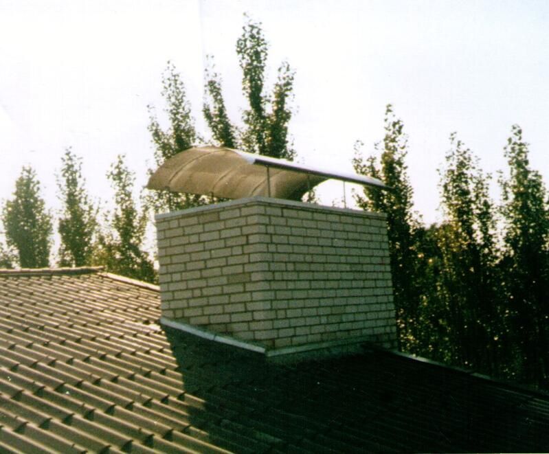 Ein gemauerter Schornstein auf einem Dach mit Bäumen im Hintergrund