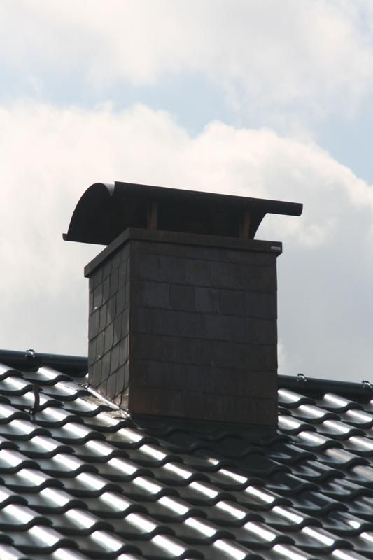 Ein Schornsteinschutz auf einem Ziegeldach mit einem bewölkten Himmel im Hintergrund