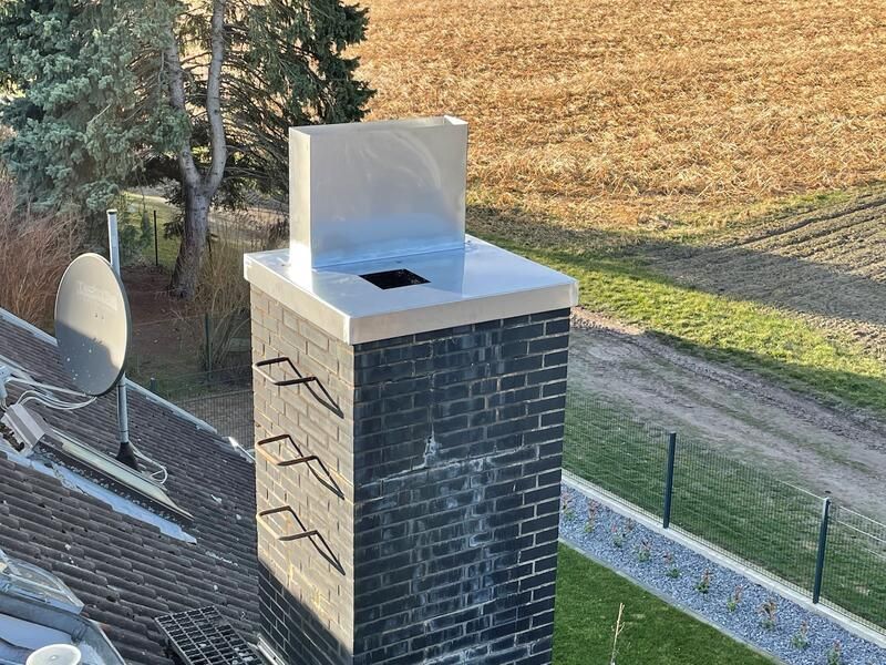 Auf einem Dach befindet sich ein gemauerter Schornstein mit einer Metallspitze.