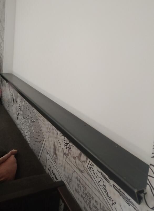 Eine Person sitzt auf einem Stuhl vor einer Wand, an der ein Regal steht.