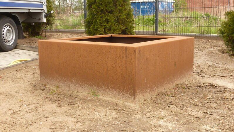 Ein großer quadratischer Blumentopf steht im Dreck neben einem Lastwagen.