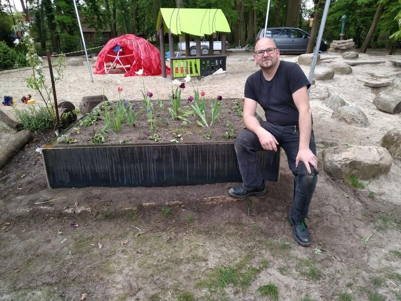 Ein Mann sitzt auf einem Felsen vor einem Garten.