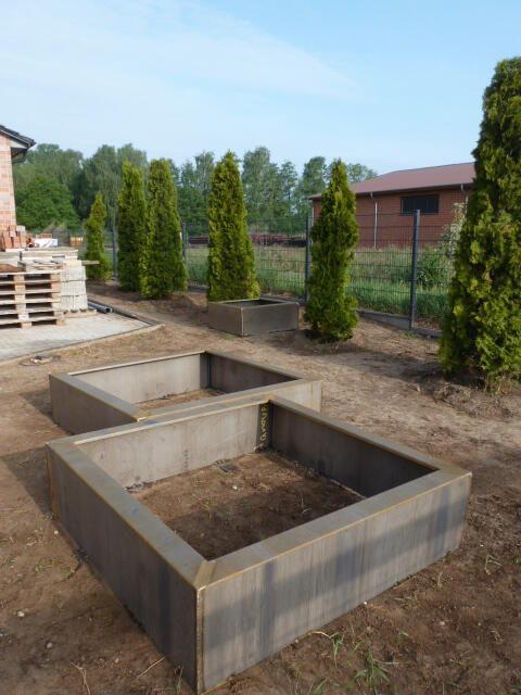 Zwei Betonpflanzgefäße stehen im Dreck vor einem Haus