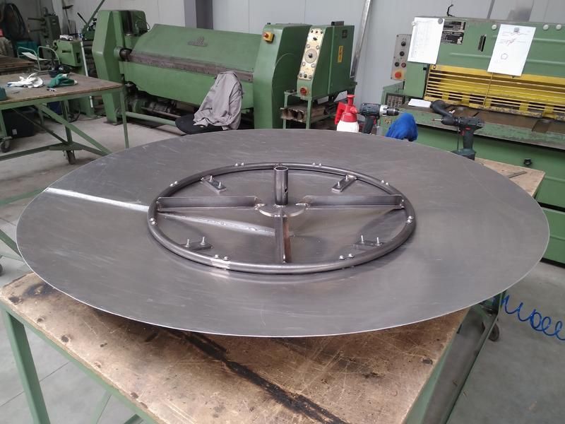 Eine große Metallscheibe liegt auf einem Holztisch in einer Fabrik.