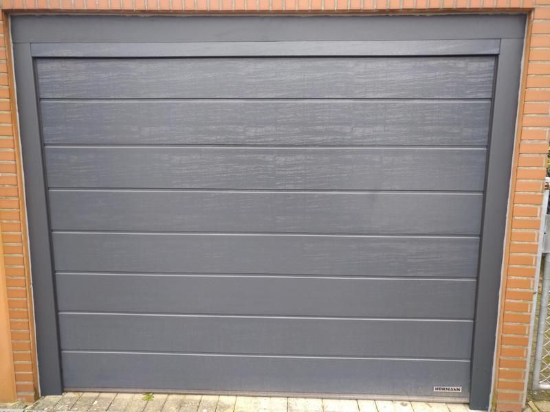 Neben einer Backsteinmauer steht ein schwarzes Garagentor.