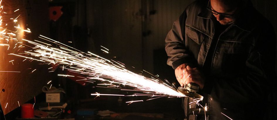 Ein Mann schleift in einem dunklen Raum ein Stück Metall.