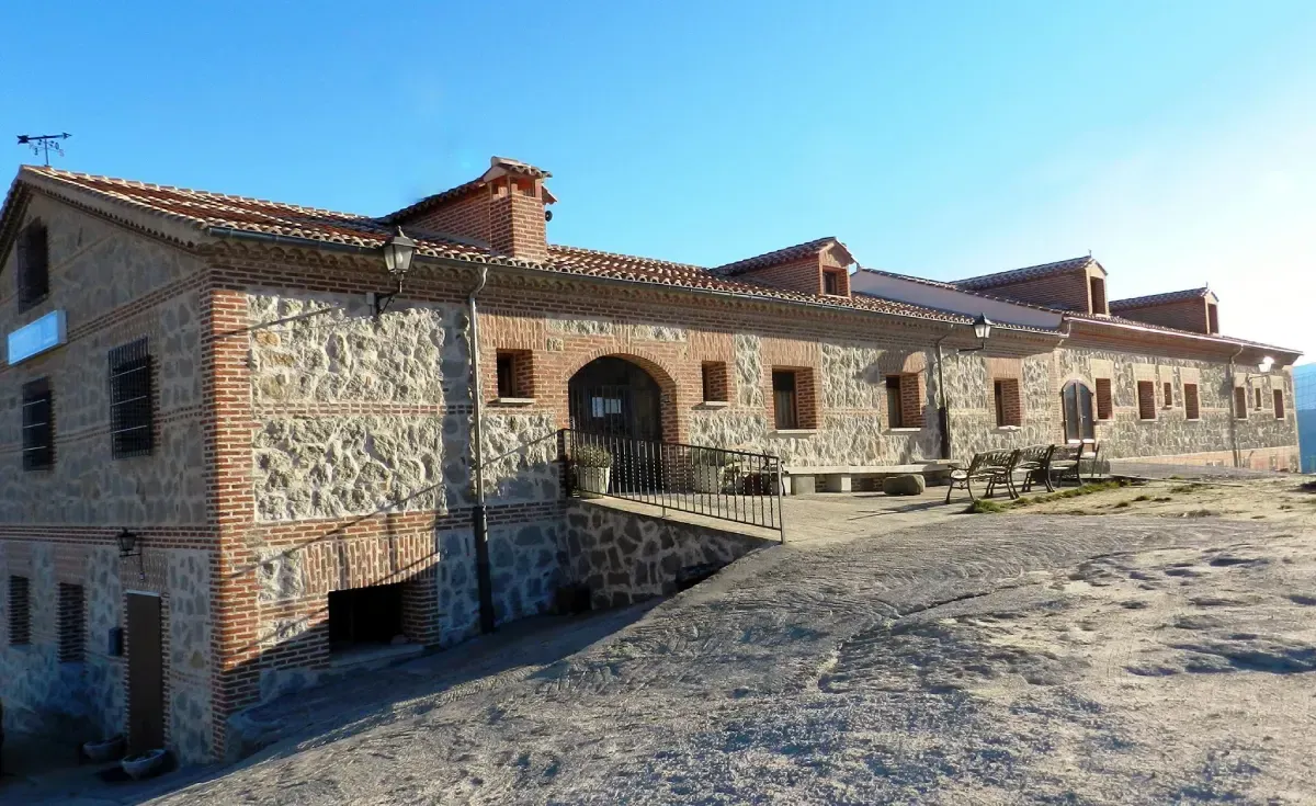 Casa de campo de piedra con tejados de tejas rojas y una pequeña rampa bajo un cielo azul claro.