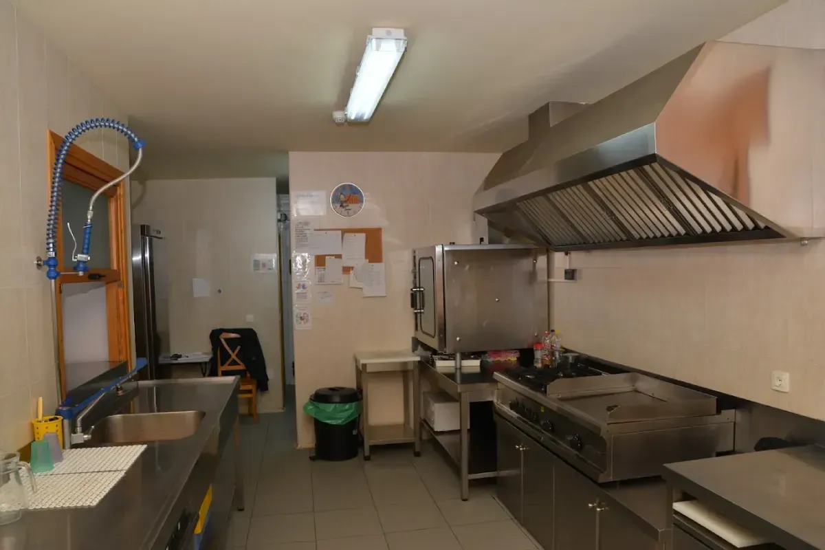 Cocina comercial con encimeras, fregadero, estufa y campana extractora de gran tamaño.