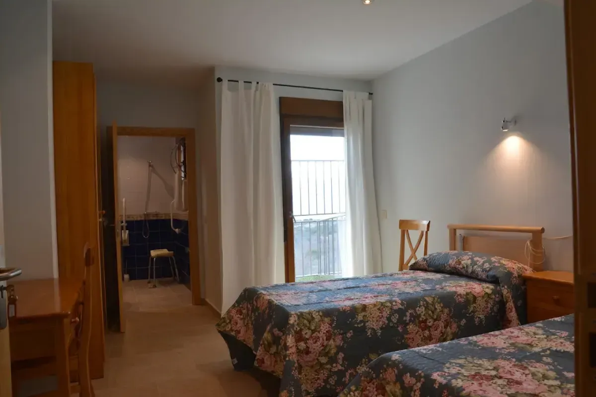 Habitación pequeña con dos camas individuales, una ventana y una puerta abierta que da a un baño.
