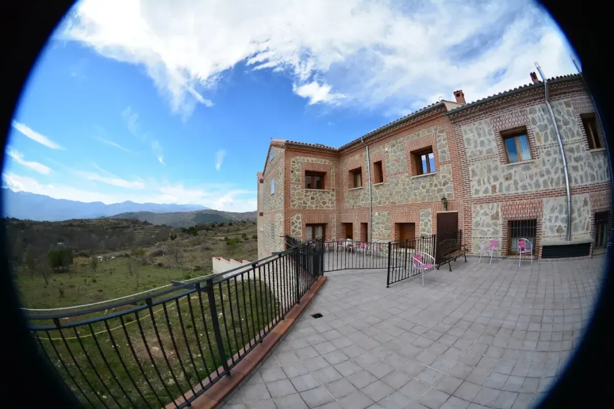 Patio de piedra junto a una casa rústica con vistas a la montaña y al cielo más allá de una barandilla negra.