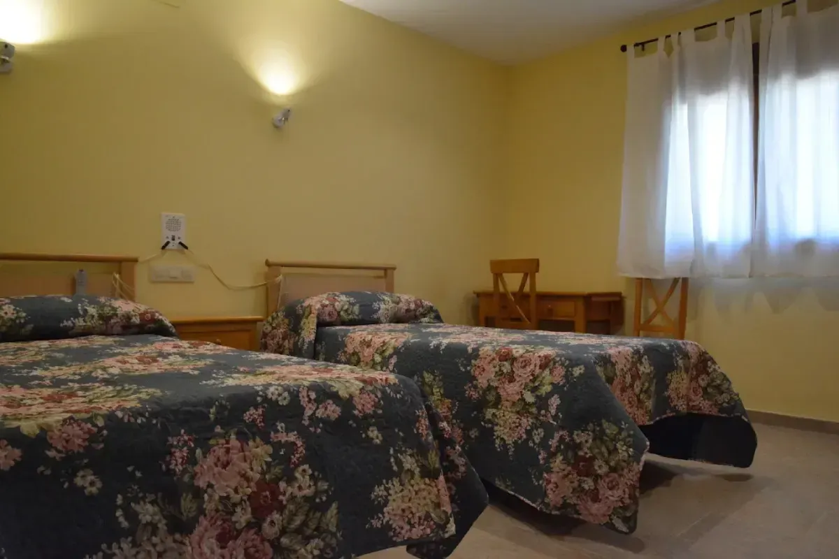 Habitación de hotel con tres camas individuales vestidas con colchas florales y cortinas blancas