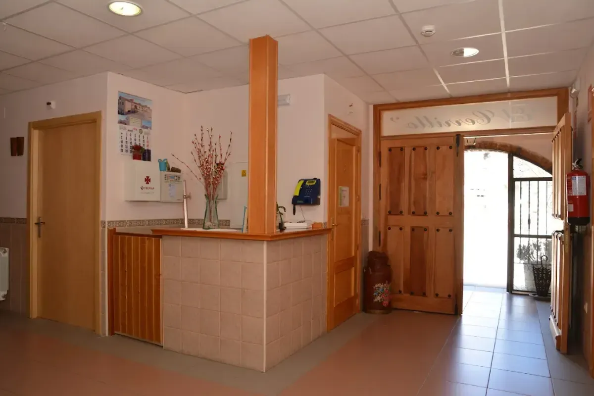 Interior de un modesto vestíbulo de oficina con mostrador de recepción de madera y entrada al pasillo.