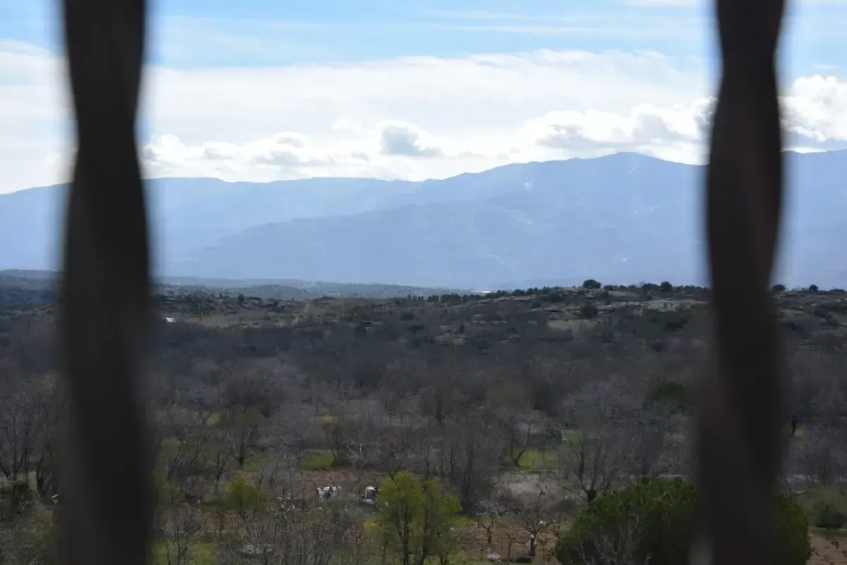 Vista a través de oscuras barras verticales de un valle brumoso y lejanas montañas azules bajo un cielo nublado.