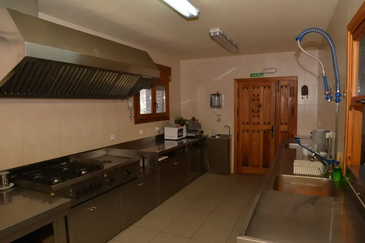 Cocina comercial con encimeras de acero inoxidable, estufa, campana extractora y armario de almacenamiento de madera.