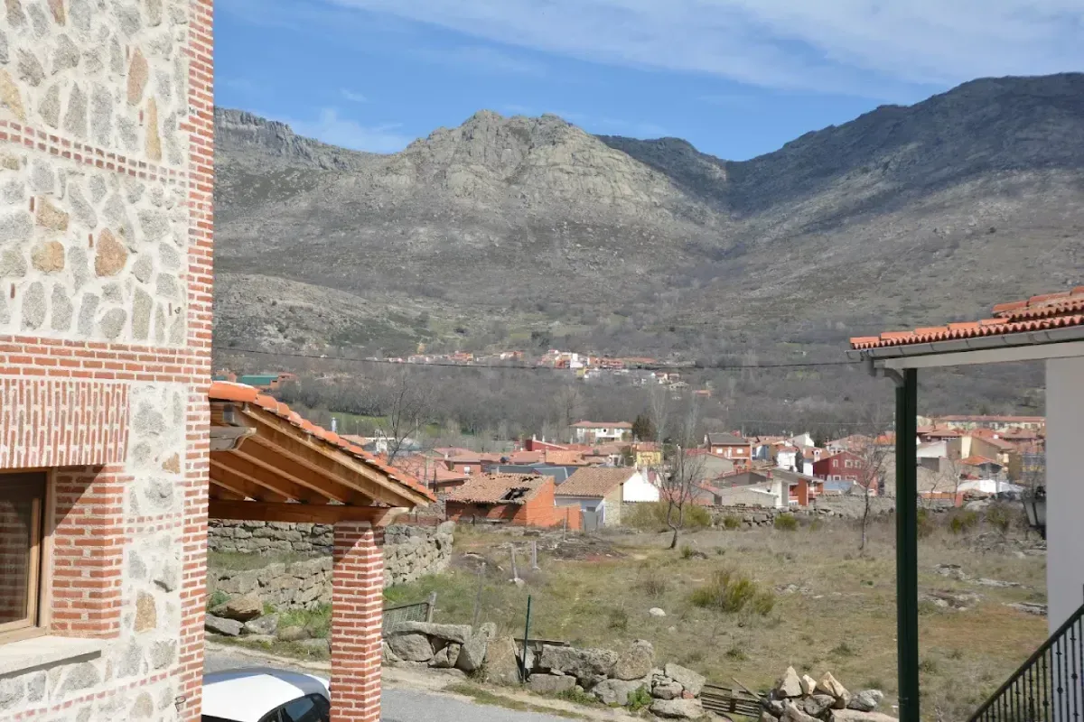 Pueblo de montaña con tejados de tejas rojas bajo colinas rocosas y un cielo azul.