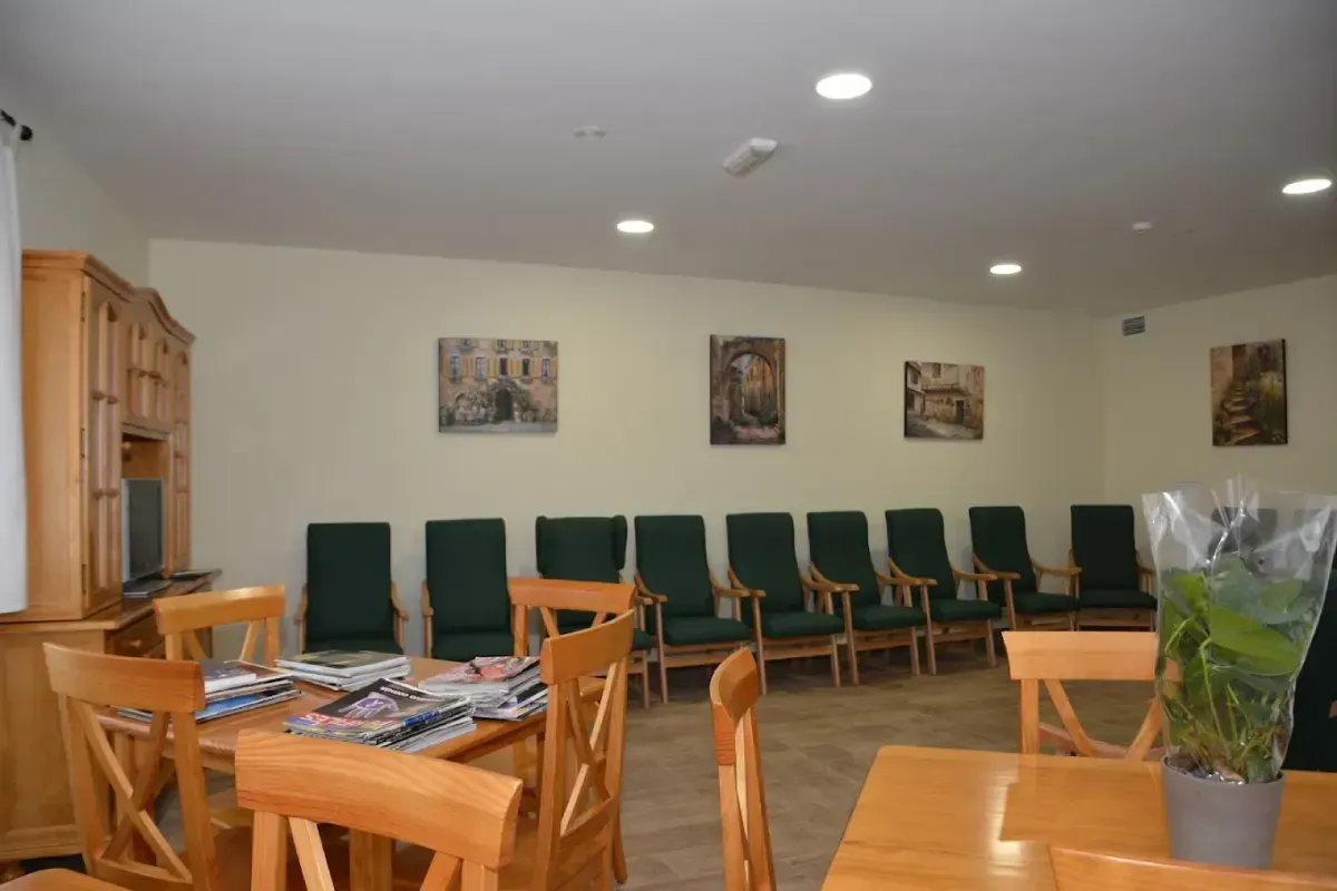 Sala de espera tranquila con sillas verdes, mesas de madera y cuadros enmarcados en las paredes