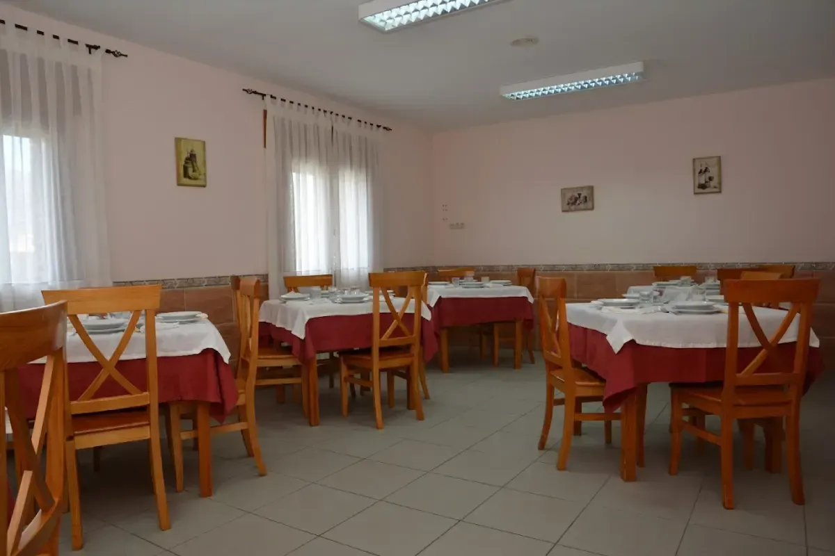 Comedor vacío con manteles rojos, sillas de madera, suelo de baldosas y luces fluorescentes en el techo.