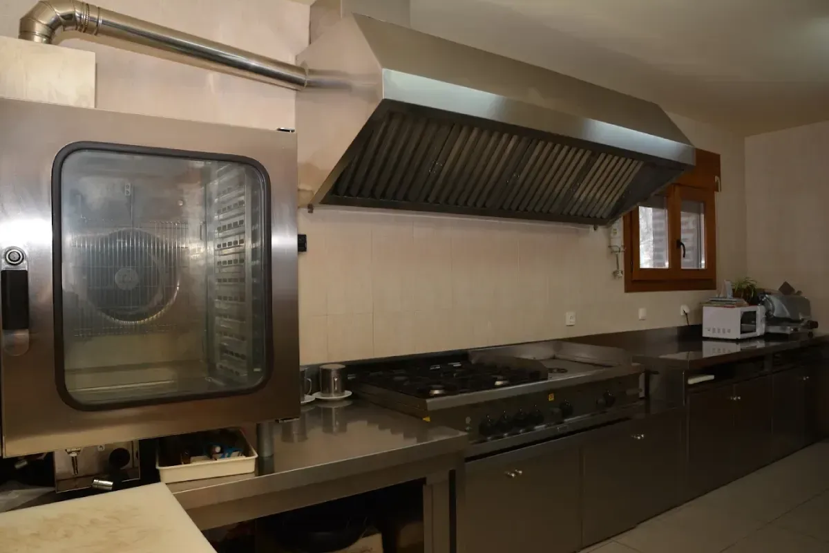 Cocina comercial de acero inoxidable con horno, estufa, campana extractora y electrodomésticos de mostrador.