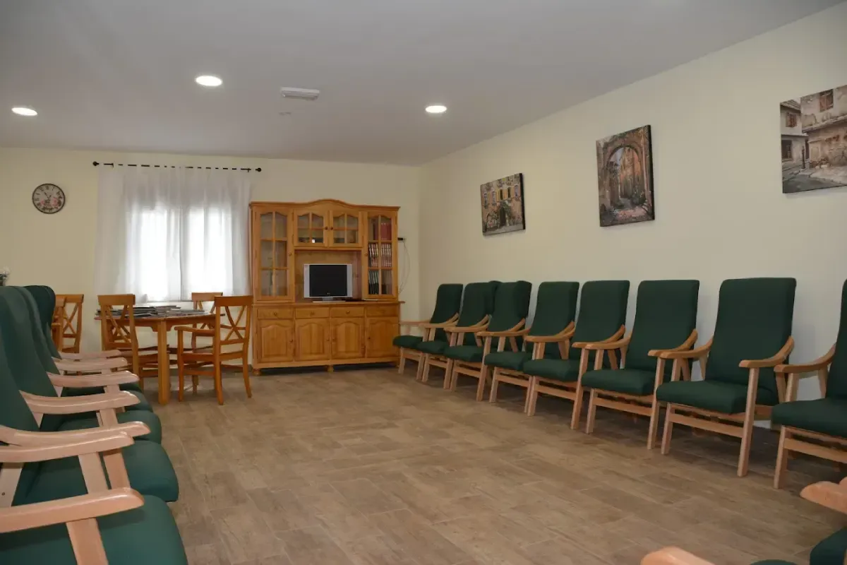 Sala de espera vacía con filas de sillas verdes y un armario de madera contra paredes de color beige.