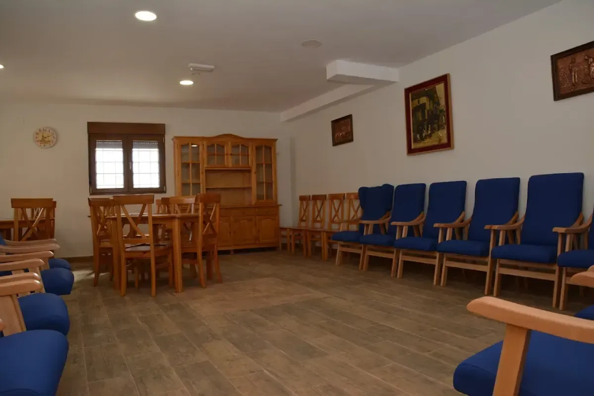 Sala de espera vacía con sillas azules, mesa y armario de madera y cuadros enmarcados en la pared.