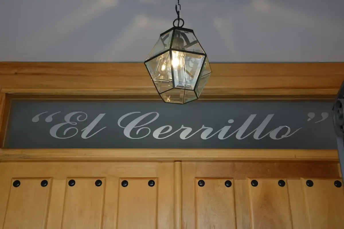 Letrero de la tienda que dice “El Cerrillo” sobre puertas de madera con una linterna colgante