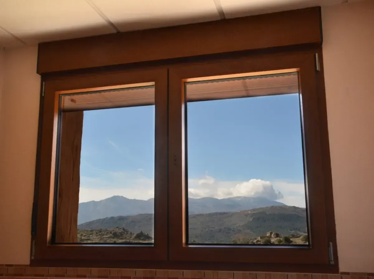 Ventana con marco de madera y vistas a la montaña y al cielo nublado.