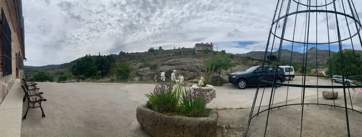 Vista de un patio con un coche azul aparcado, bancos, un parterre de flores y un edificio en la cima de una colina