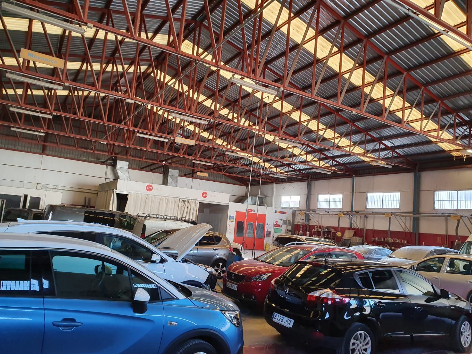 Autos dentro de un taller con techo metálico alto. Se ven varios vehículos.