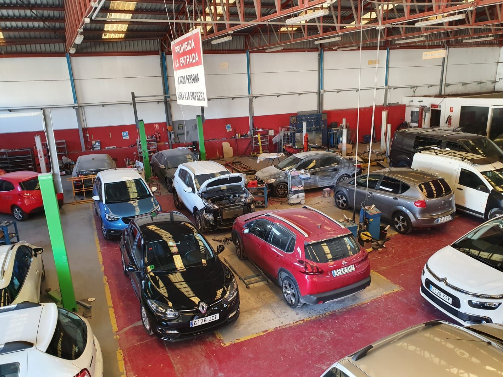 Automóviles en varios estados de reparación dentro de un concurrido taller de reparación de automóviles con elevadores y herramientas.