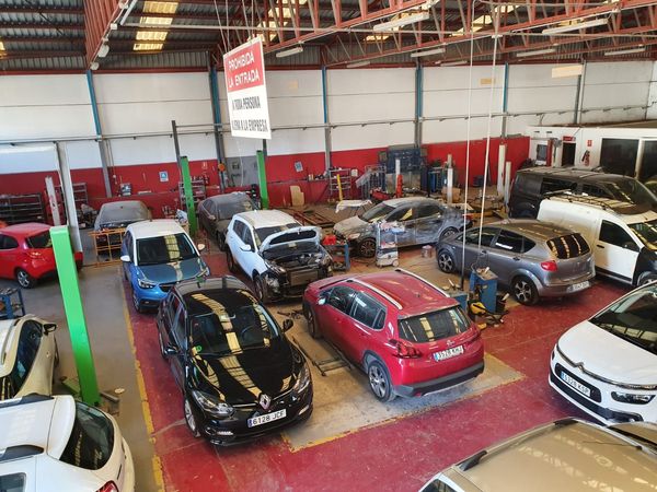 Automóviles en varios estados de reparación dentro de un concurrido taller de reparación de automóviles con elevadores y herramientas.