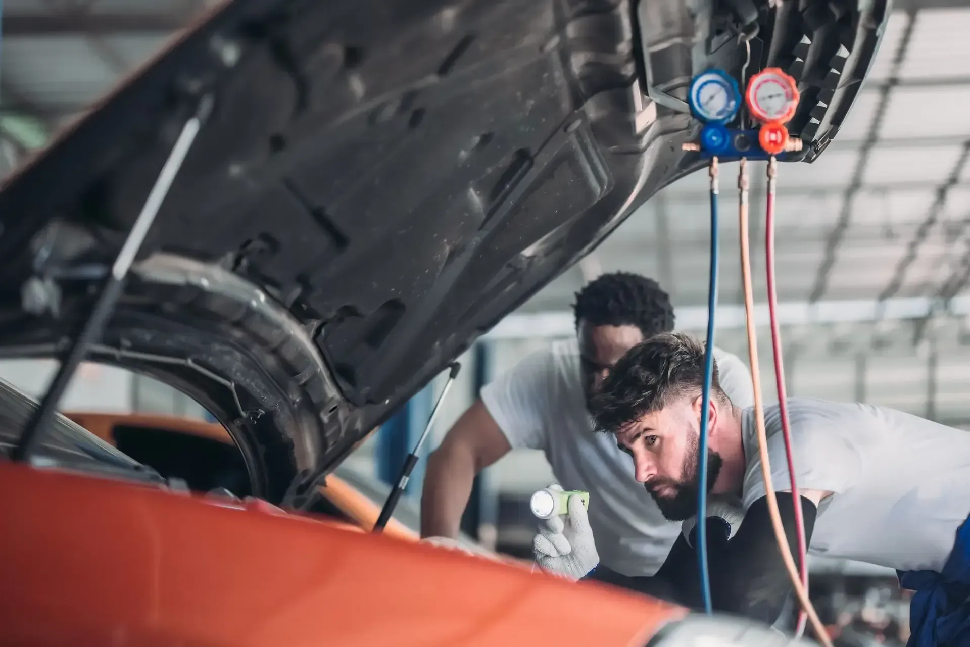 Dos mecánicos trabajan en el motor de un coche bajo el capó en un taller. Se han instalado indicadores.