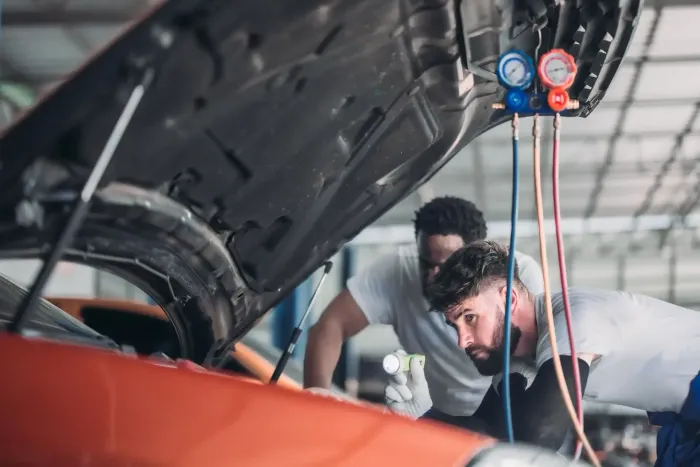 Dos mecánicos trabajan en el motor de un coche bajo el capó en un taller. Se han instalado indicadores.