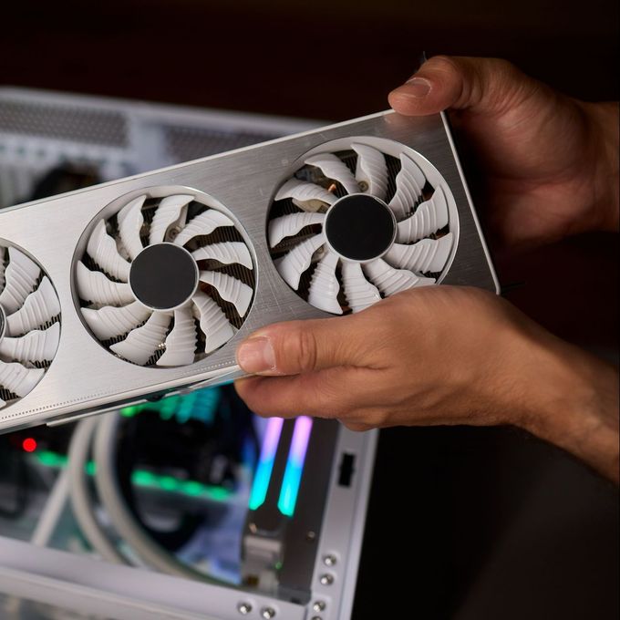 Une personne tient une carte graphique devant un ordinateur