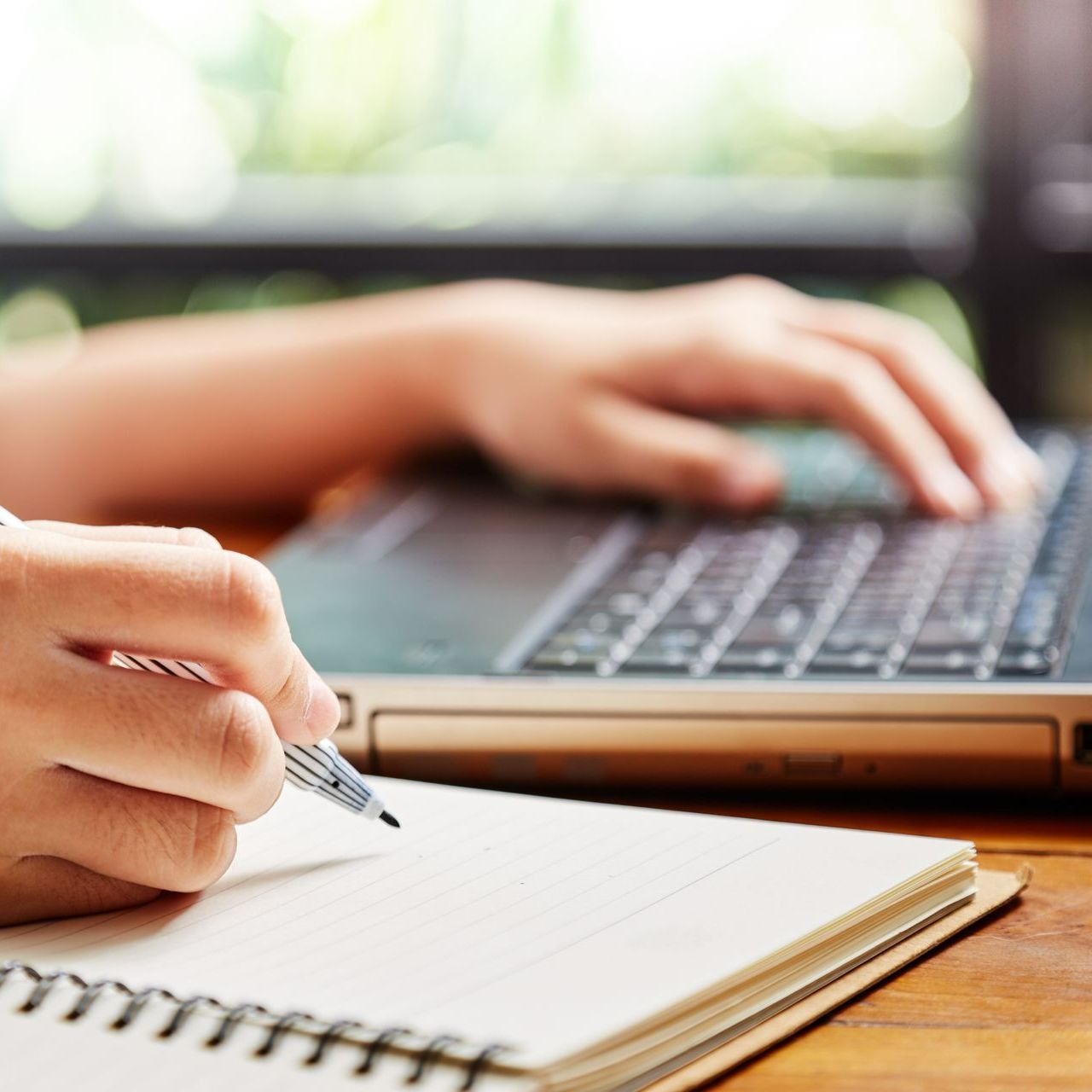 Une personne écrit dans un cahier tout en tapant sur un ordinateur portable