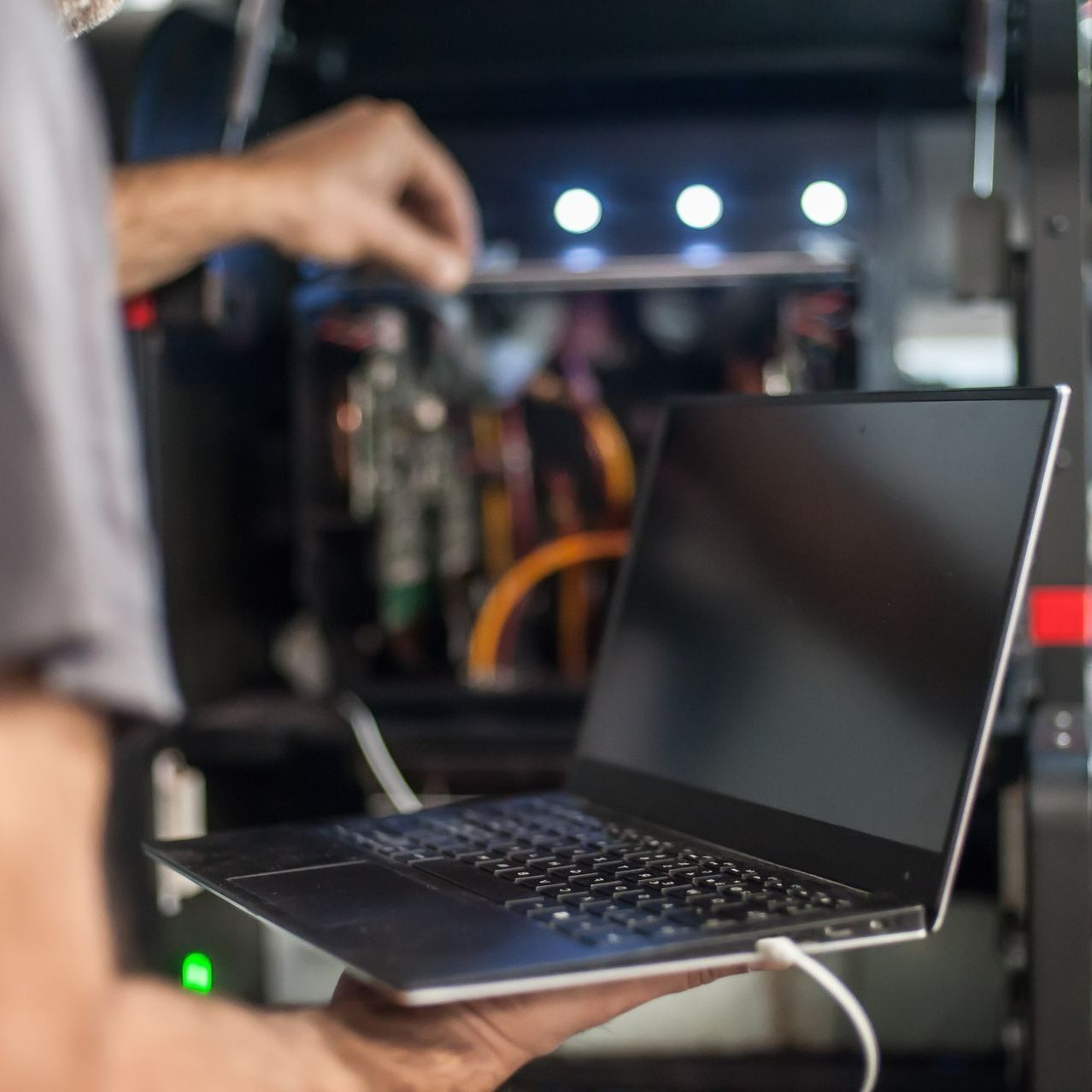 Un homme tient un ordinateur portable devant un serveur.