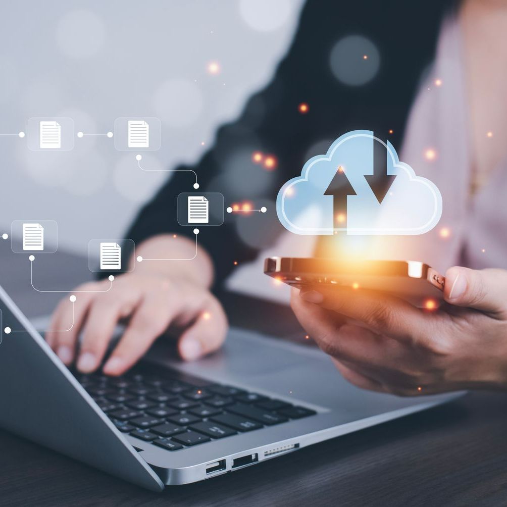 Une personne tape sur un ordinateur portable et tient un téléphone portable d'où sort un nuage.