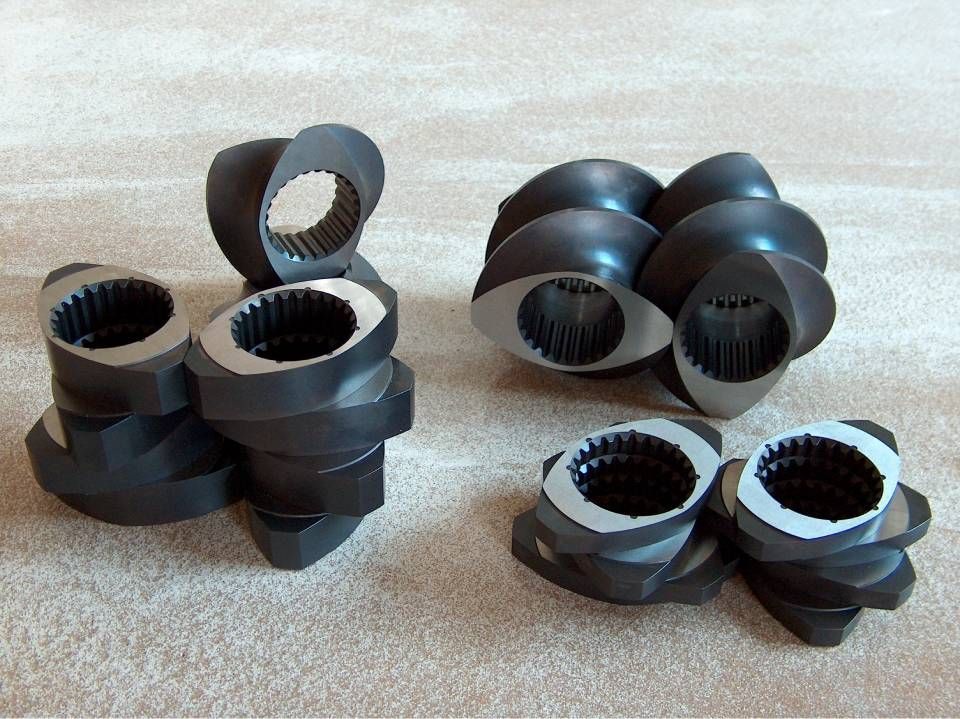 Nahaufnahme mehrerer dunkler Metall-Extruderschneckenelemente, die auf einer Oberfläche angeordnet sind.