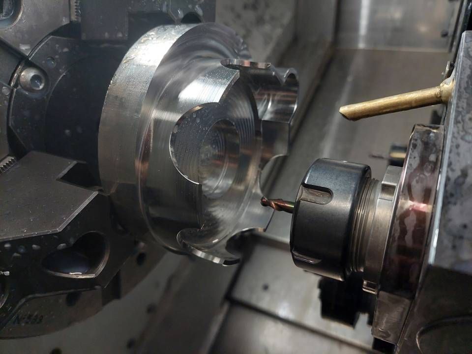 CNC-Maschine schneidet ein Metallteil; Werkzeuge und Kühlmittel sind sichtbar.