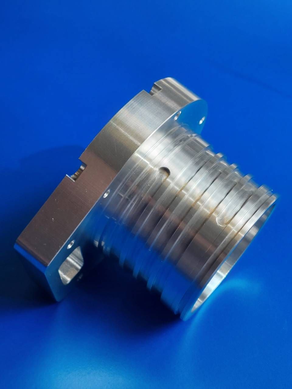 Ein silberfarbenes, maschinell bearbeitetes Metallteil auf blauem Hintergrund mit zylindrischen Rippen und kantigen Merkmalen.