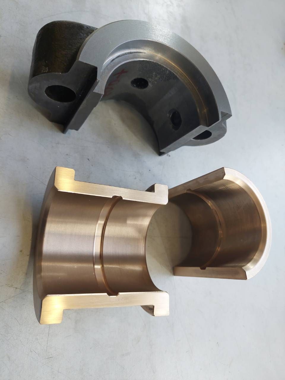 Zwei halbkreisförmige Metallteile, eines schwarz und eines bronzefarben, für Maschinen, möglicherweise Lager.