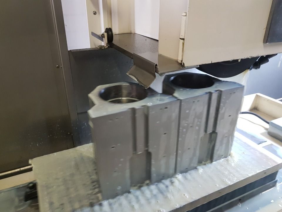 Ein Metallblock wird von einer CNC-Maschine bearbeitet, Kühlmittel ist sichtbar.